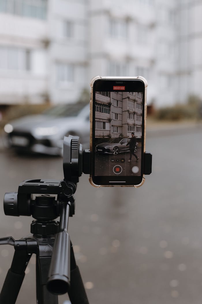 A smartphone on a tripod capturing an urban environment with a person walking by.