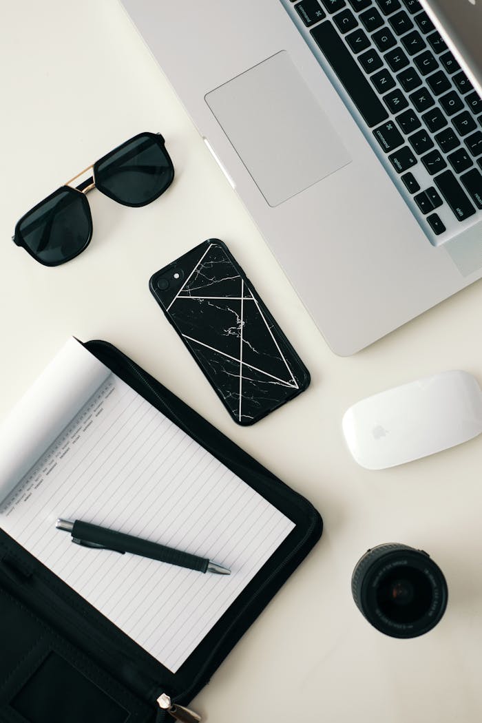 Services-02 A clean workspace featuring a laptop, smartphone, sunglasses, and stationery on a white surface.