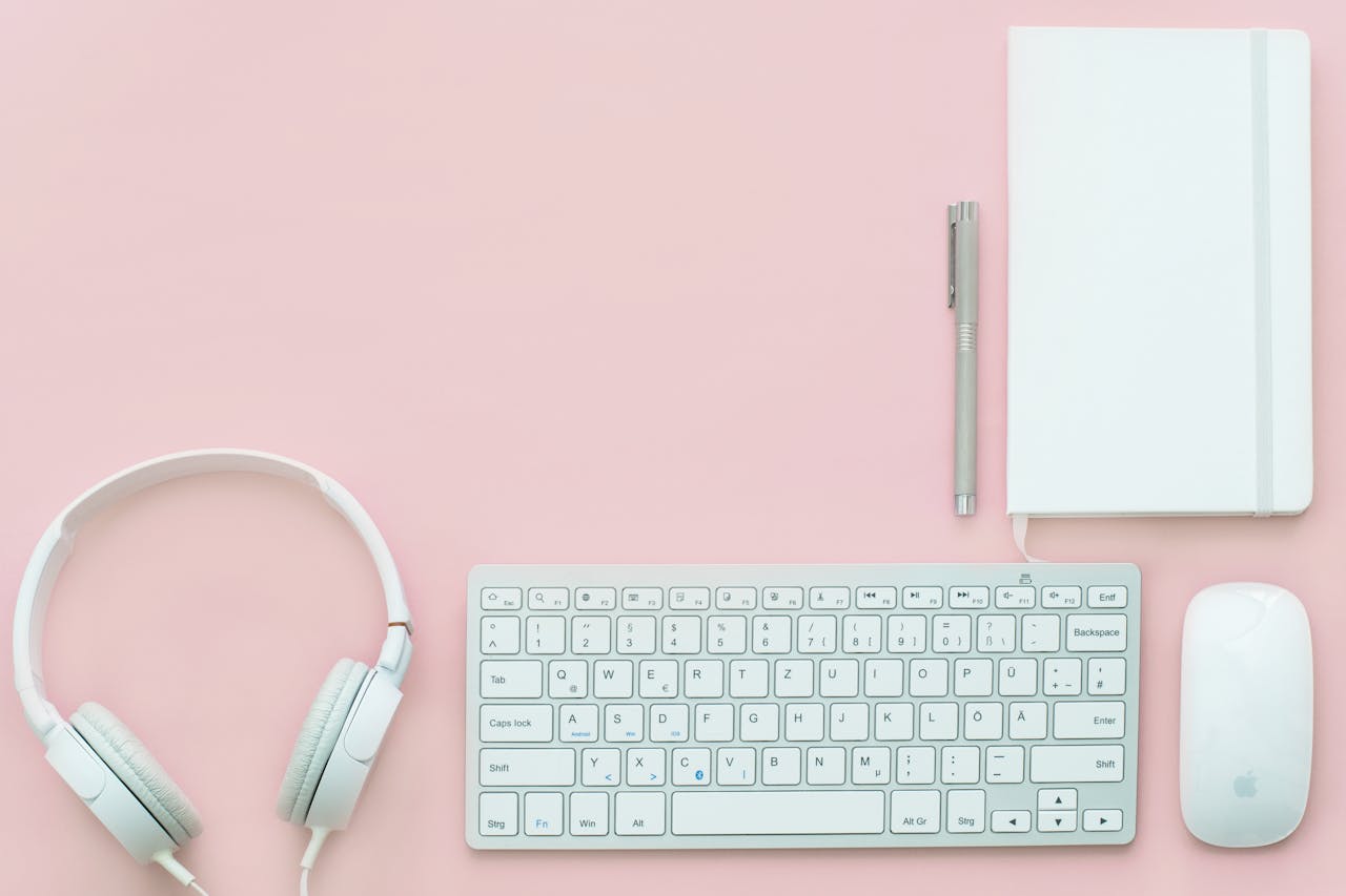 creative Flat lay of modern workspace with keyboard, mouse, headphones on pink background.