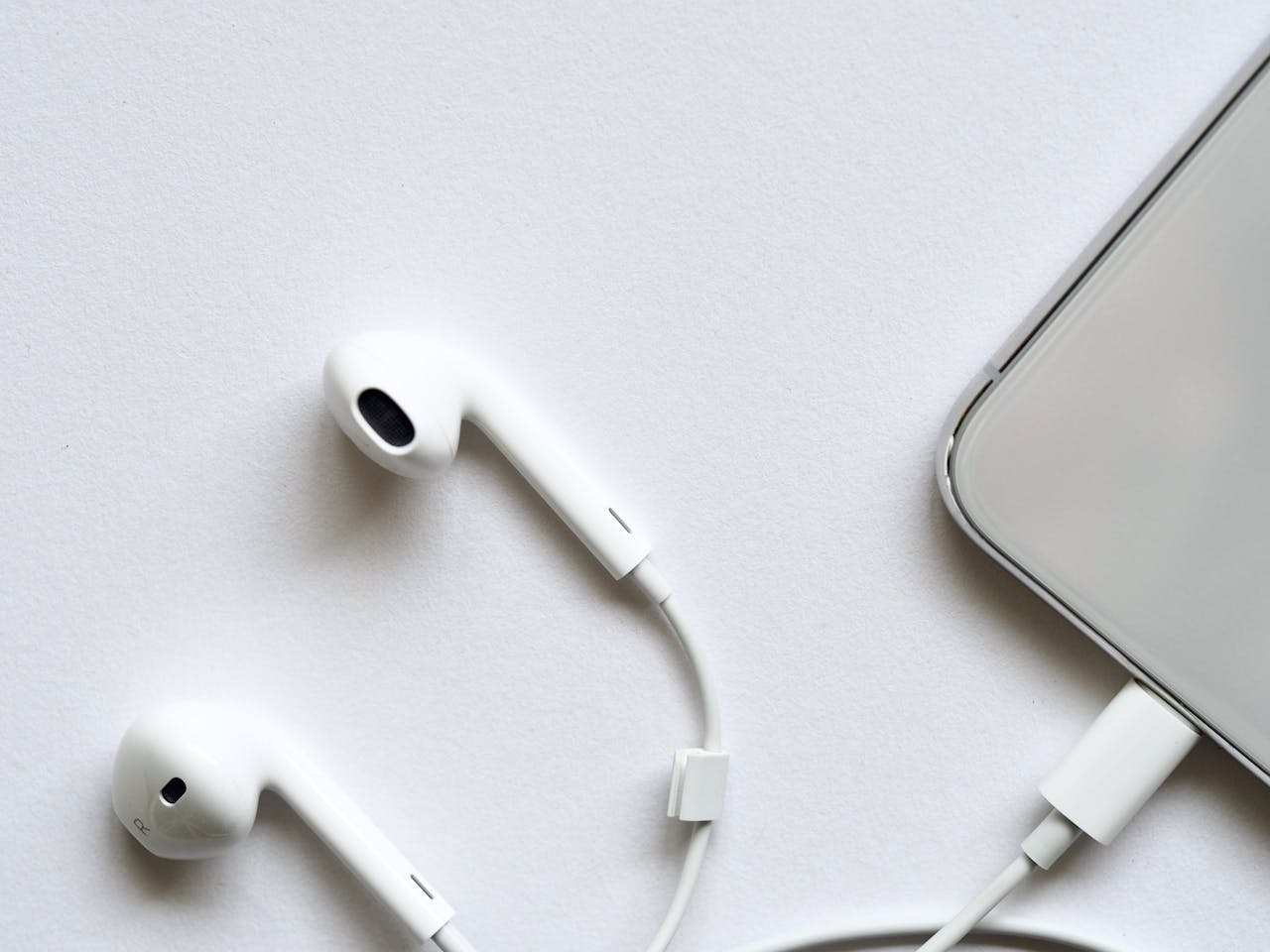digital Minimalist top view of white wired earphones connected to a smartphone on a clean white background.